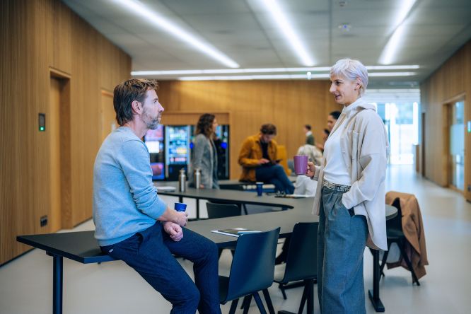 Studierende, angelehnt an Tischen, unterhalten sich im Foyer des Traktes U. Im Hintergrund sind Kaffee- und Getränkeautomaten zu sehen.