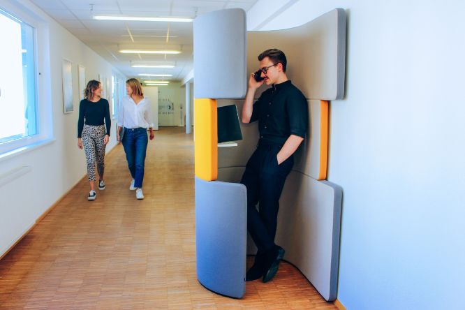 Ein Student telefoniert in der Telefonzelle. Zwei Studentinnen gehen am Gang vorbei