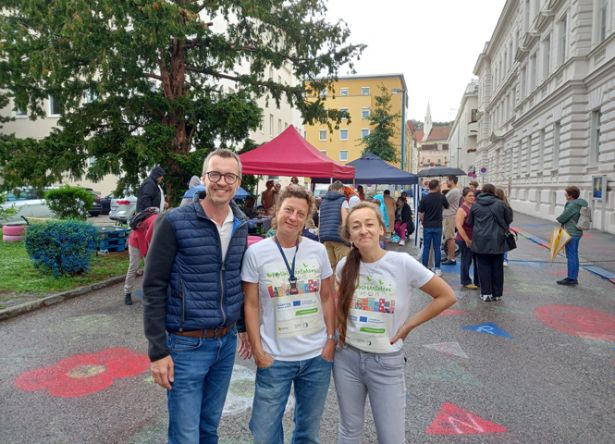 3 Personen im Vordergrund vor Hafnerplatz mit Zelt