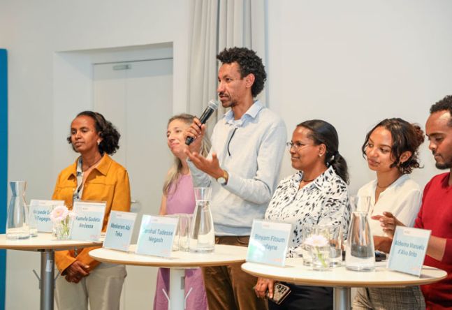 Projektpartner stehen bei Stehtischen und beantworten Fragen aus dem Publikum