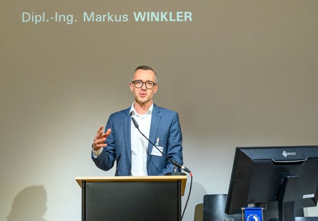 Mann mit blauem Anzug und weißem Hemd vor beigem Hintergrund