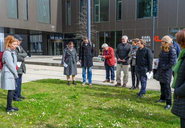 Gruppe steht vor Grünfläche und unterhält sich darüber