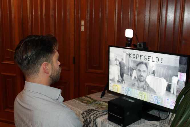 KOPFGELD Installation - Person vor einem Bildschirm, der eine Banknote zeigt mit einem Gesicht, das der Person ähnelt