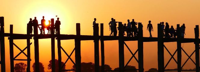 Image of the PhD Program shows humans standing on a bridge in the light of sunset or sunrise