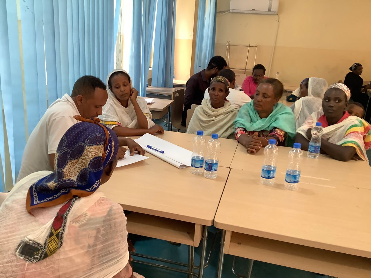 Menschen sitzen um zwei zusammengeschobene Schulbänke, auf denen Mineralwasserflaschen stehen