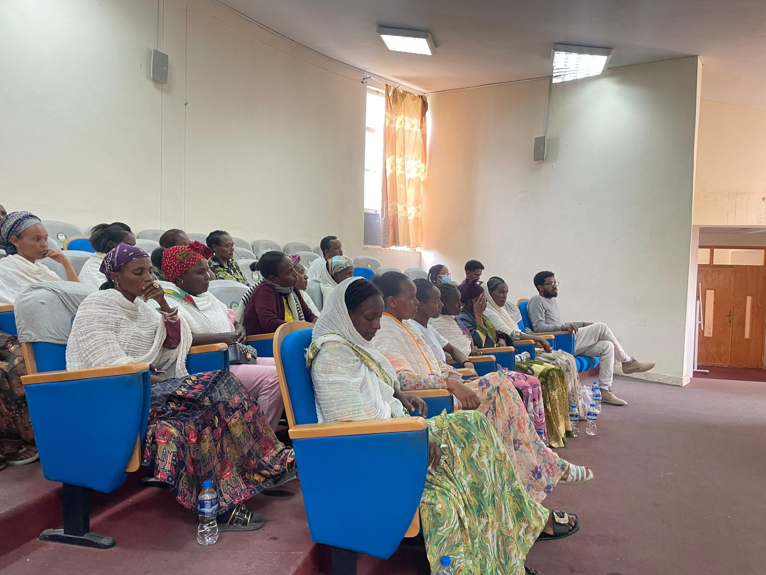 afrikanische Frauen in bunten Gewändern auf blauen Sesseln in Hörsaal