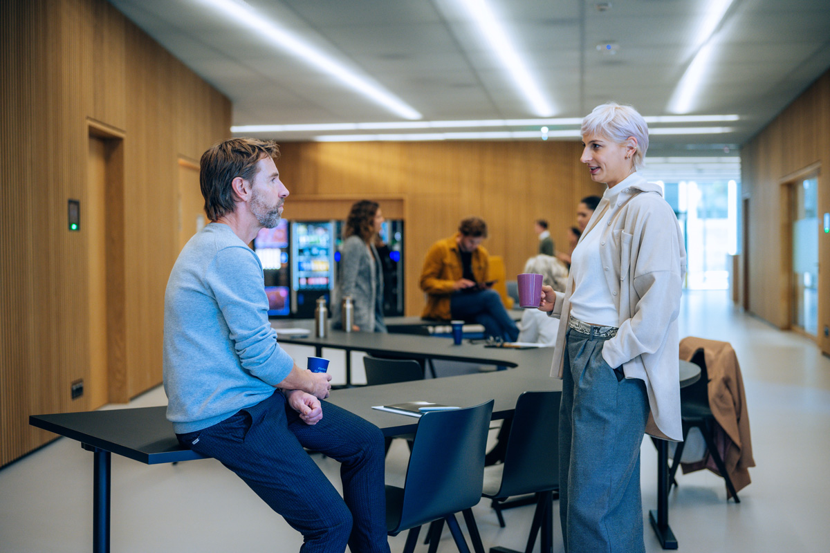 © Walter Skokanitsch Studierende, angelehnt an Tischen, unterhalten sich im Foyer des Traktes U. Im Hintergrund sind Kaffee- und Getränkeautomaten zu sehen.