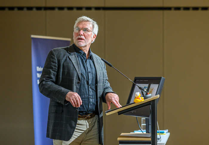 Mann in grünem Sakko und beiger Hose bei Rednerpult