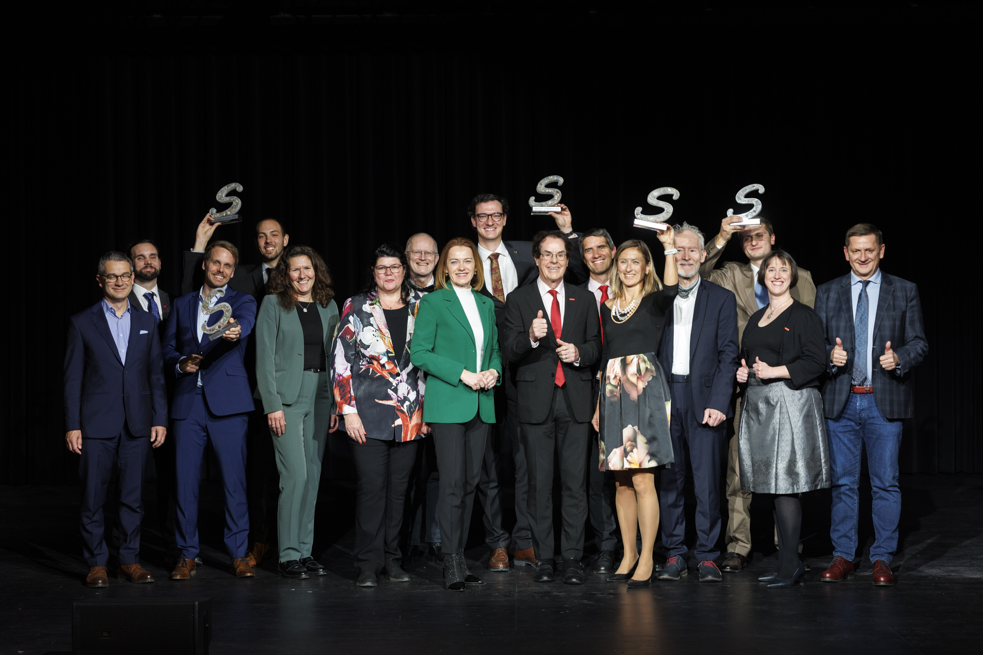 Gruppenbild mit allen Siegern und Jury vor schwarzem Hintergrund