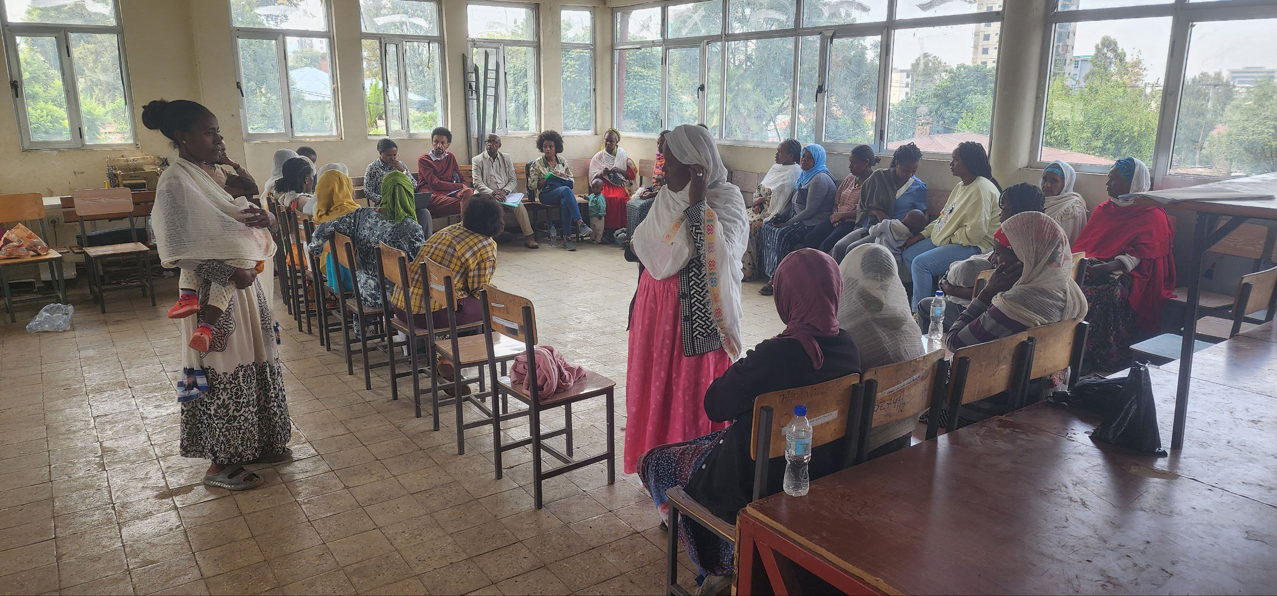 colorfully dressed African women sit on chairs in a circle in a hall