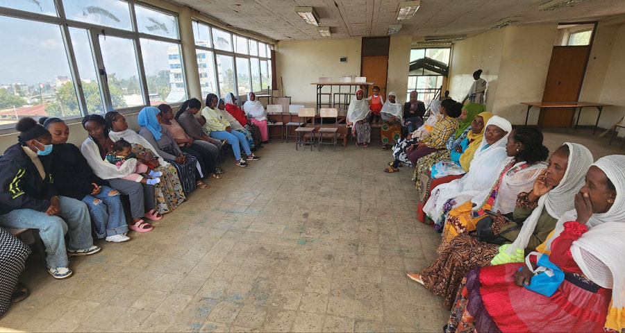 colorfully dressed African women sit in a semicircle in a hall