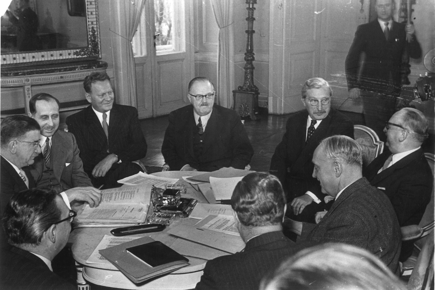 Schwarzweiß-Bild mit Männern in Anzügen um runden Tisch